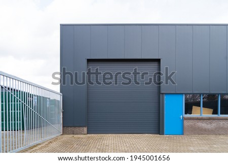 small industrial warehouse with roller doors and blue entrance door Royalty-Free Stock Photo #1945001656