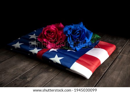 FOLDED FLAG OF THE UNITED STATES OF AMERICA WITH TWO ROSES, ONE RED AND ONE BLUE. HONORS AND MILITARY TRIBUTE TO THE FALLEN SOLDIERS.
MEMORIAL DAY CONCEPT.
 Royalty-Free Stock Photo #1945030099