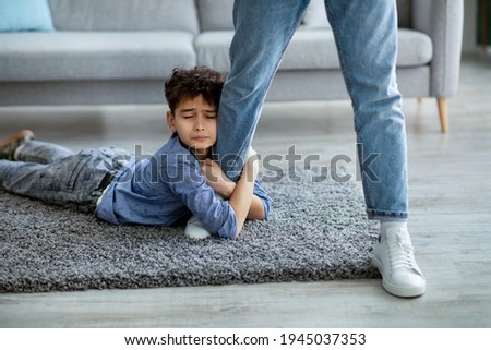 Don't go, dad. Upset boy embracing his father leg, begging daddy to stay with him, lying on the floor carpet. Sad son holding man and close eyes Royalty-Free Stock Photo #1945037353