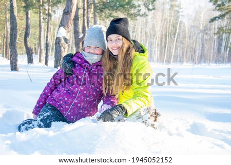 In winter, on a bright sunny day in a snowy forest, girlfriends girls play near a large snowdrift.