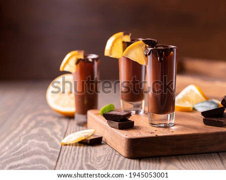 Cocktail in shot glass with chocolate, cream liqueur, fresh oranges on dark background. Homemade shot drinks party. Bar menu, recipes. Close up, selective focus