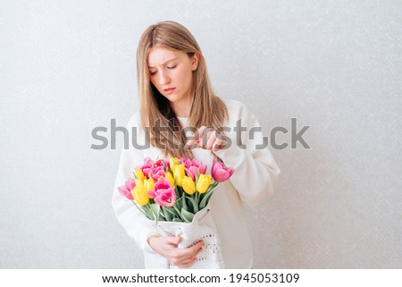 Portrait of sad young caucasian woman with long hair, holding bouquet of pink and yellow tulip flowers. White background, copy space, close up.