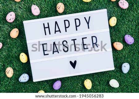 The inscription HAPPY EASTER on a background of grass and colorful eggs. Easter eggs on a green background. Ready-made postcard and background for a festive theme.