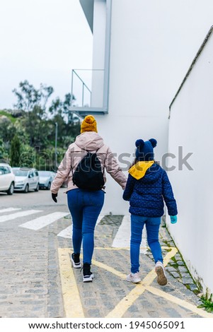 mother and daughter hand in hand with their backs to each other in winter clothes walking in the street