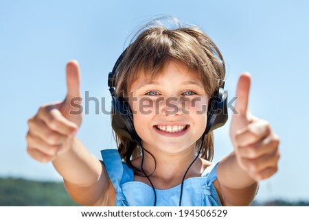Happy little girl in headphones listens to music against the blue sky