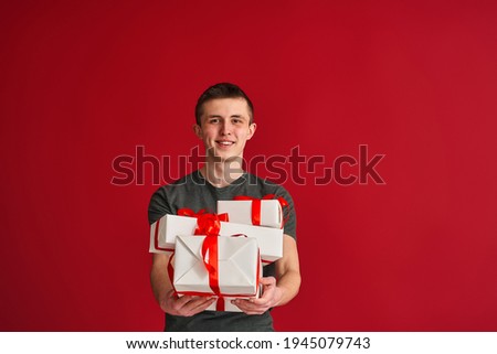 young teenager in casual clothing holds a lot of white gift boxes with red ribbons and holds them forward on a red background. The concept of giving gifts, winning