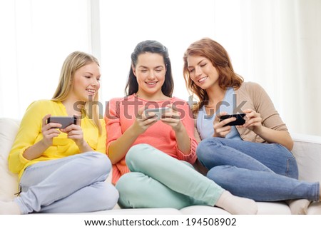 friendship, technology and internet concept - three smiling teenage girls with smartphones at home