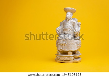 Sitting small emperor sculpture figurine in stately seat with white space. Studio souvenir still life against a seamless yellow background.