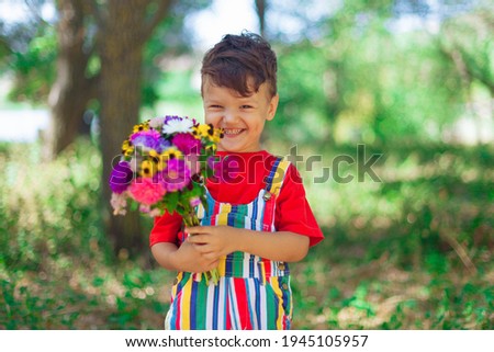Laughing boy with a bouquet of wild flowers in his hands against the background of nature. Mother's Day. A child with bright flowers in bright clothes laughs and rejoices. Lifestyle