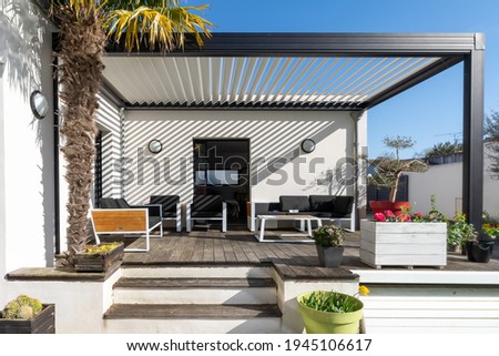 Trendy outdoor patio pergola shade structure, awning and patio roof, garden lounge, chairs, metal grill surrounded by landscaping Royalty-Free Stock Photo #1945106617