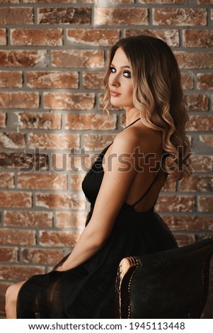 Side view of a model girl with perfect evening makeup wearing a black dress against the brick wall