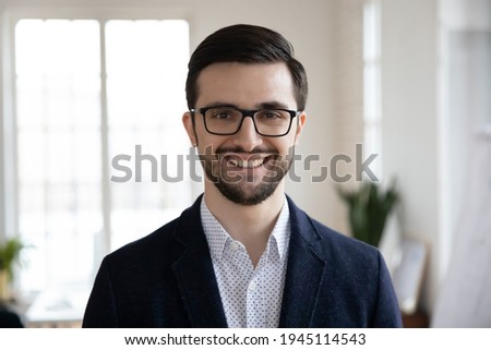 Profile picture of smiling young Caucasian businessman in suit and glasses pose in modern office. Headshot portrait of happy confident successful male boss or CEO at workplace. Employment concept.