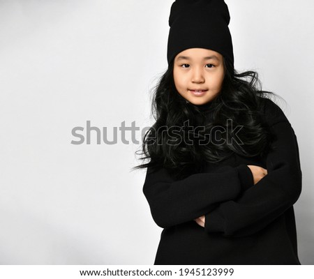 Hipster Asian girl with black curls in a hat, folded her arms over her chest and looks boldly at you