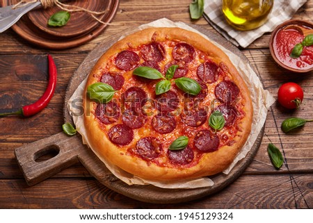 Pepperoni pizza. American style homemade pizza with salami, mozzarella cheese and tomato sauce. Freshly baked and served with basil leafs.