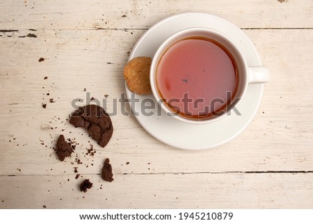 Background photo with a white cup of tea with a saucer and round cracked cookies on an old wooden table with peeling paint. Chocolate and butter cookies. Bitten biscuits. Top view