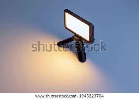 Small-sized LED lamp for photo and video production. It stands on a tripod, is illuminated and illuminates. Soft focus.