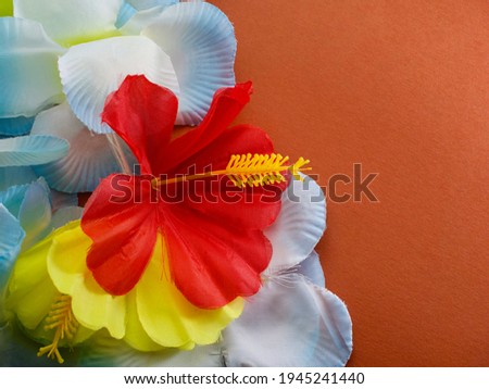 Isolated fake light blue Hawaiian lei with red and yellow hibiscus flowers against brown background