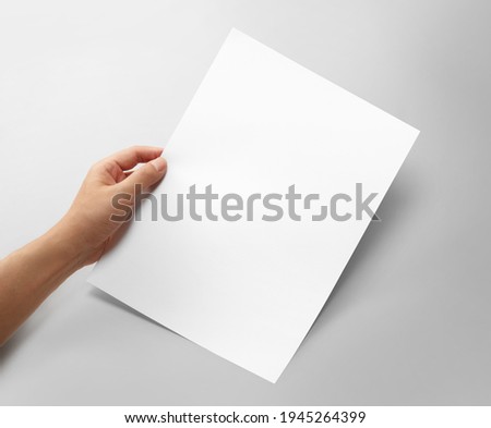 Hand holding a blank a4 size paper isolated on grey background. Royalty-Free Stock Photo #1945264399