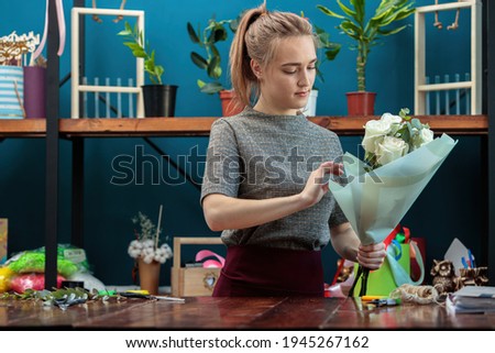 Young adult girl florist makes a bouquet of white roses.