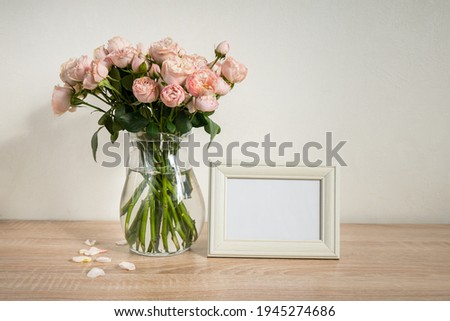 Portrait white picture frame mockup on wooden table. Modern ceramic vase with roses. White wall background. Scandinavian interior. 