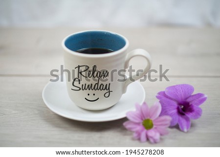 Relax Sunday. Sunday concept with happy smile on cup of morning coffee closeup and pink purple flowers on white table bright background. Happy relax Sunday weekend.
