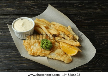 Baking paper with fried chips and fish on wooden background