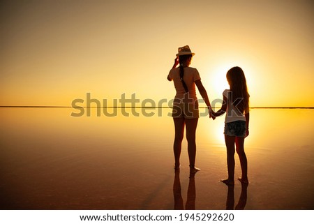 Two happy lovely sisters are walking along the mirror salt lake enjoying the evening fiery sunset