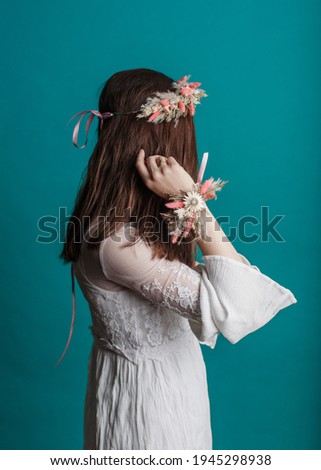 
Young hipster girl in a white dress with a wreath of dried flowers on her hand. Dry herb trendy decoration