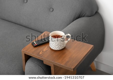 Cup of tea with remote control on armrest table in room Royalty-Free Stock Photo #1945310707