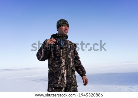 a man in military clothes holds binoculars in his hand and looks.  In the background snowy steppe and blue sky.