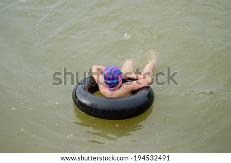 small girl with diving hat floating on an inflatable tire in water pond surface 
