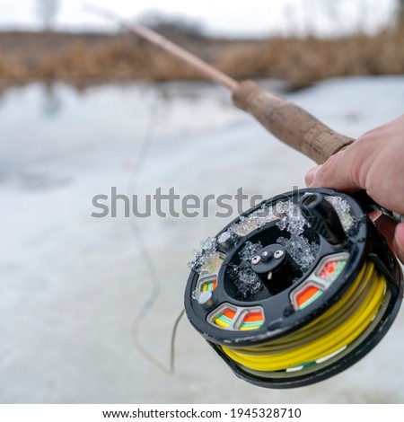 Photo winter fly fishing picture. Fly rod and reel on snowy river bank.