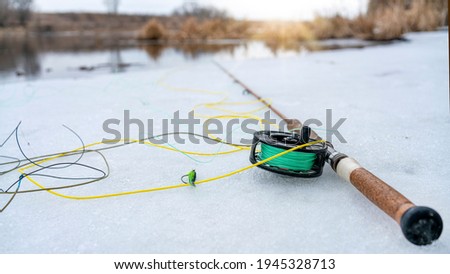 winter fly fishing picture. Fly rod and reel on snowy river bank.
