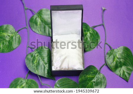 Black gift box pictured with purple background and decorative leaves