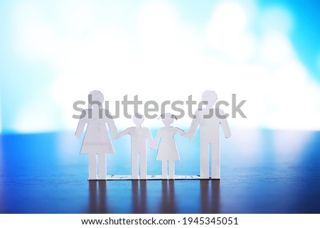 Cutout paper chain family with the protection of cupped hands, concept for security and care. Hands with cut out paper silhouette on table. Family care concept