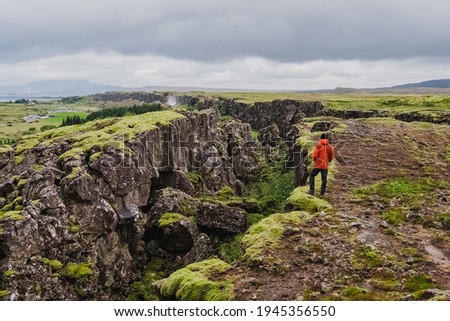 A man in a red jacket stands in Tingvelir National Park in Iceland. Fracture of tectonic plates. Panoramic photo. It is the site of a rift valley that marks the crest of the Mid-Atlantic Ridge. 