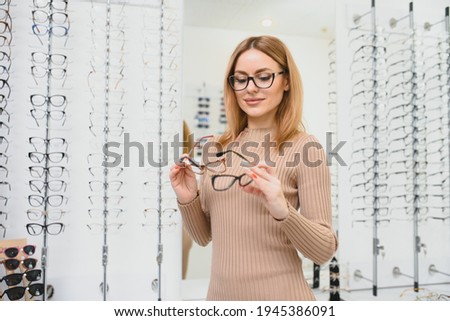 Health care, eyesight and vision concept - happy woman choosing glasses at optics store. Portrait of beautiful young woman trying new glasses in optician store Royalty-Free Stock Photo #1945386091