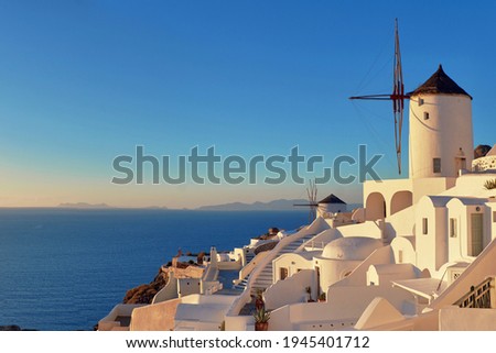 Sunset over Santorini island in Greece. Traditional church, apartments and windmills in Oia village, panoramic image.