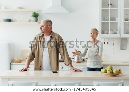 Quarrel at home, screams, angry couple, family problems and scandal during covid-19 lockdown. Upset middle aged husband and wife quarrel in kitchen interior, man ignores lady arguments, empty space