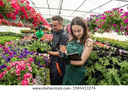 Young male and female florists with clipboard communicating while analzying stock of plants in a greenhouse.