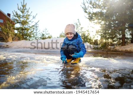 preschooler boy is playing with a stick in brook on sunny day. Child having fun and enjoy a big puddle.All kids love play with water.Happy childhood. Outdoor activity for baby in early sping time