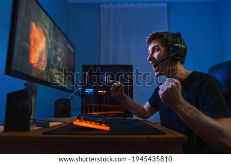 Cybersport young pro gamer happy with winning the game, feel exited, show YES hand gesture, celebrates victory in online game competition. Side view. Guy playing video game at home in his room Royalty-Free Stock Photo #1945435810
