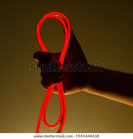 Flexible red led tape neon in hand on black background.