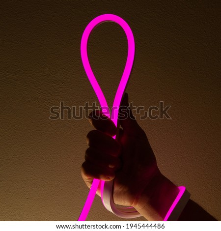 Flexible purple led tape neon in hand on black background.