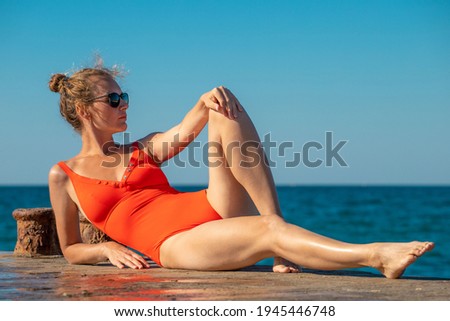 young woman in a red swimsuit on the sea pier against the background of the azure sea