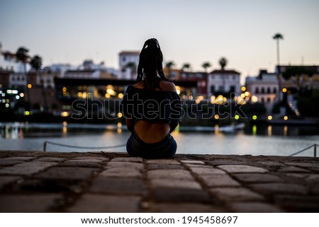 Black woman from behind sitting on night city background