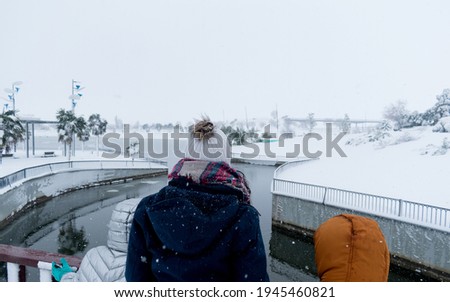 family looking from a bridge at the snowy lake on a gray day of intense snowfall