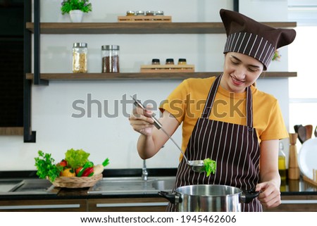 Beautiful cute Asian women standing smiling holding ladle. Housewife chef with apron cooking meat steak and salad in house kitchen for sell food box online and delivery. Work from home covid concept