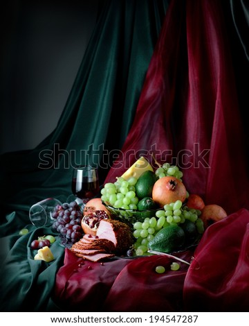 Classic still life with pomegranates, grapes, avocados and ham on a silver tray, vertical format