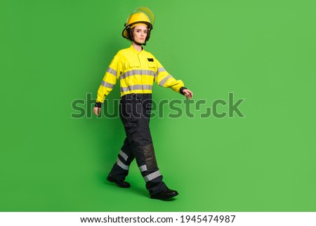 Full length photo of sweet serious young firewoman dressed yellow uniform helmet walking isolated green color background